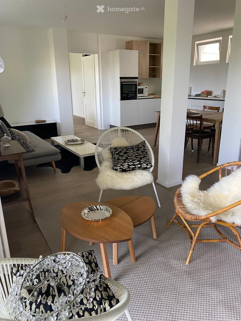 Open living space with light colors, carpet, rattan and wicker furniture, dining table with chairs, kitchen with built-in oven and microwave, hallway leading to additional rooms