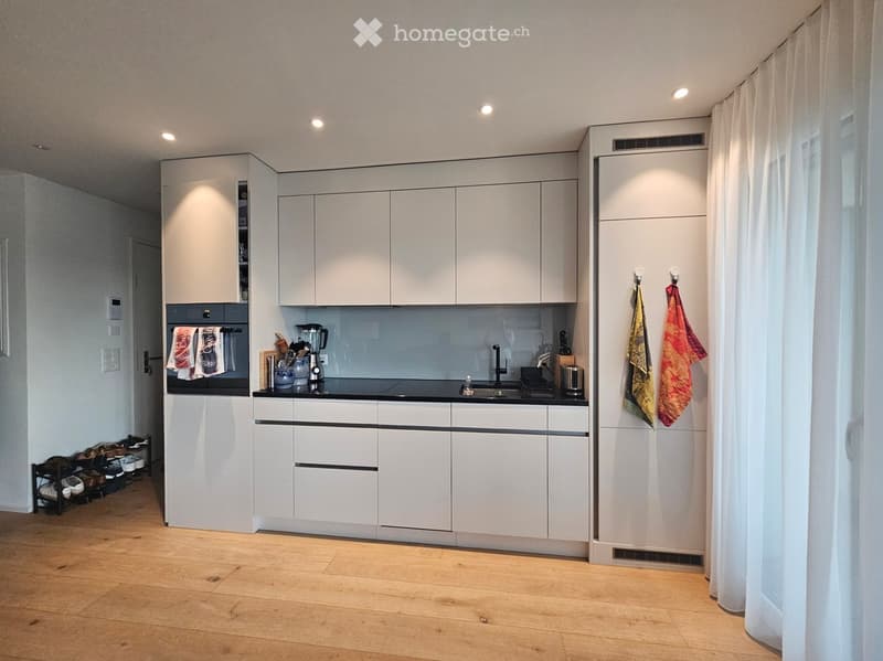 Modern kitchen with white cabinets, black countertops, and stainless steel appliances. Features include a refrigerator, oven, sink, and various kitchen utensils.