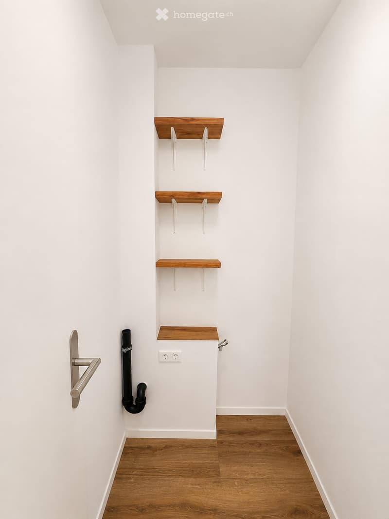 Empty room with white walls, wooden floor, and built-in wooden shelves with metal brackets. No furniture or personal items present.