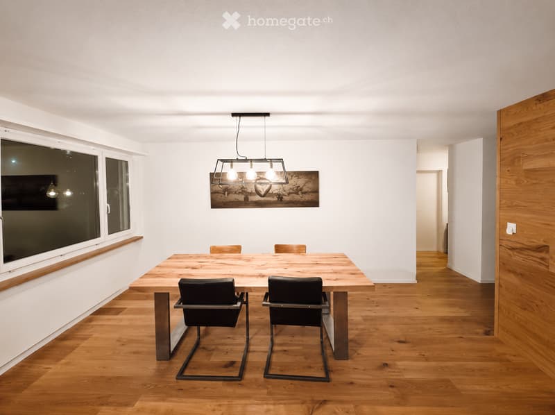 Modern dining room with a wooden table, four chairs, pendant light, and a large window with a view.
