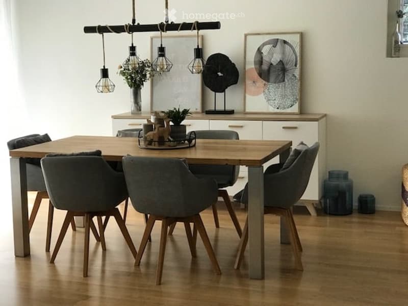 Modern dining area with a wooden dining table, six grey upholstered chairs, a white cabinet with glass doors, and decorative items including a vase with flowers and artwork on the wall.
