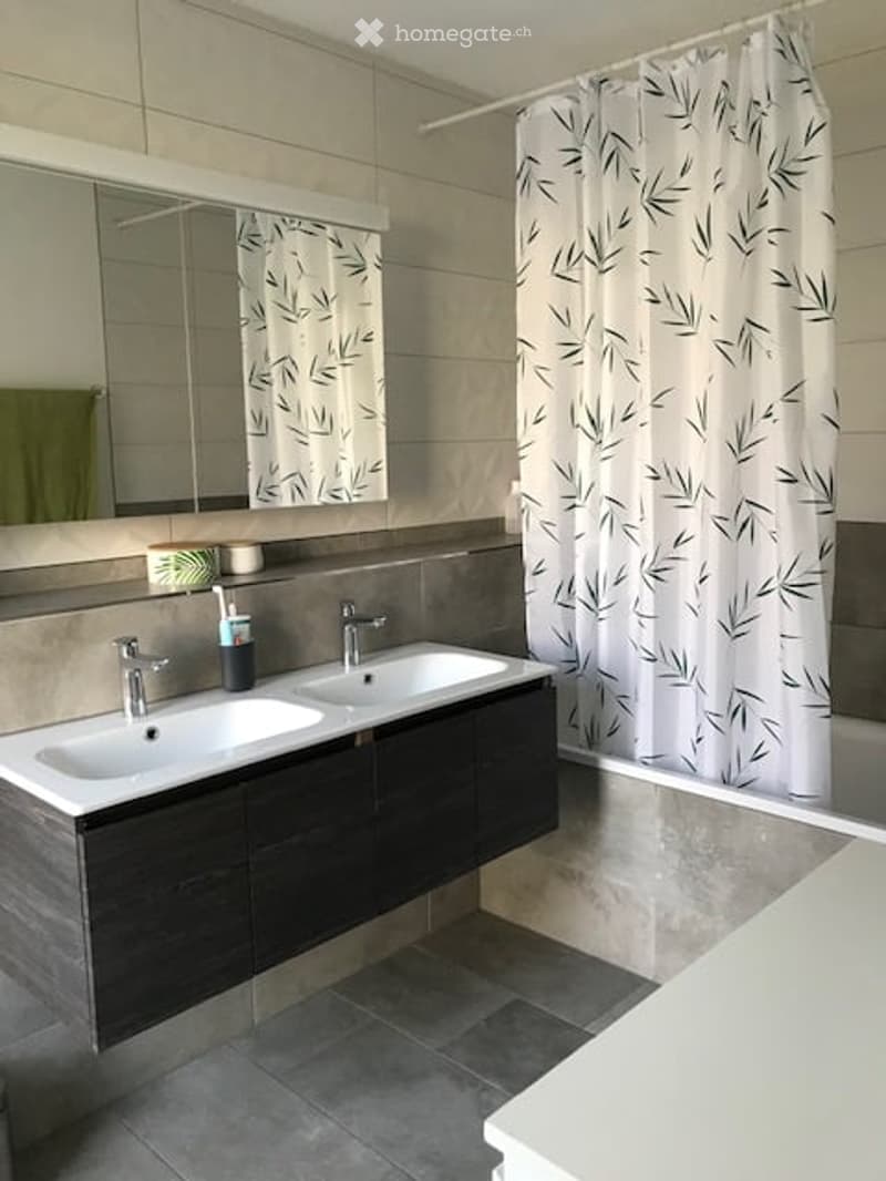 Modern bathroom with double sink, dark wooden vanity, large mirror, and leaf-patterned shower curtain.