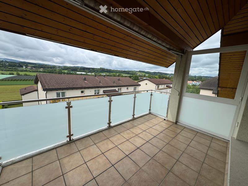 Balcony with tiled floor, glass railing, and scenic countryside view.