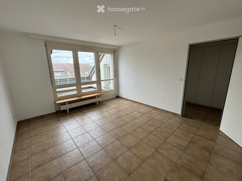 Empty room with tiled floor, large window with bench, and a closed door.