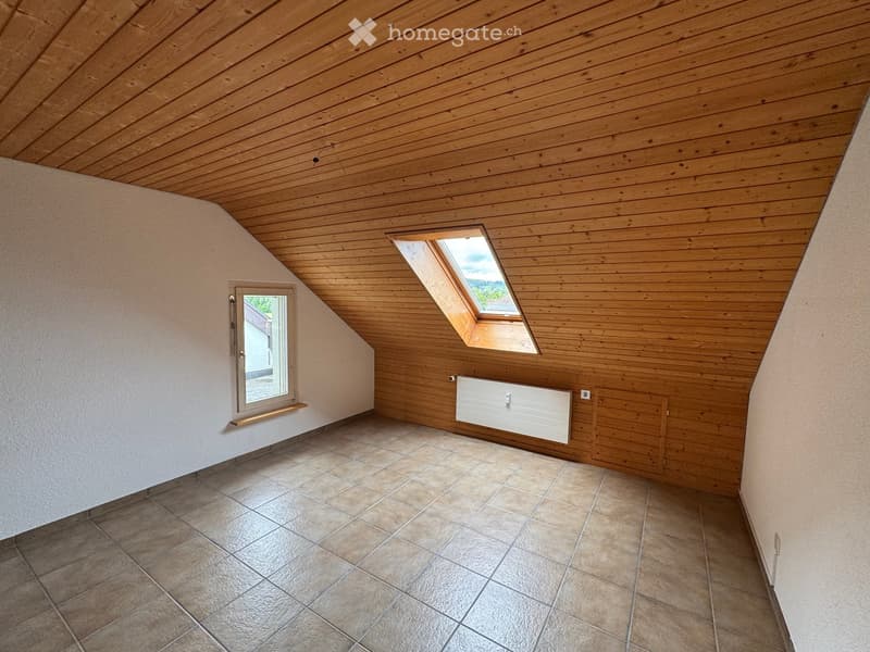 Empty attic room with wooden walls and ceiling, tiled floor, two windows, and a radiator.