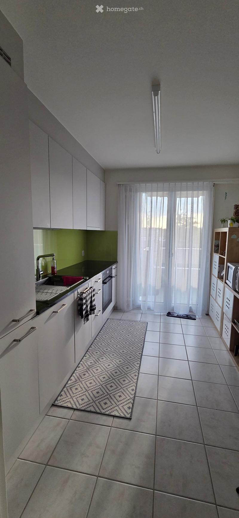 Modern kitchen with white cabinets, a black countertop, a sink with a faucet, an oven, a microwave, and a patterned rug on the floor.