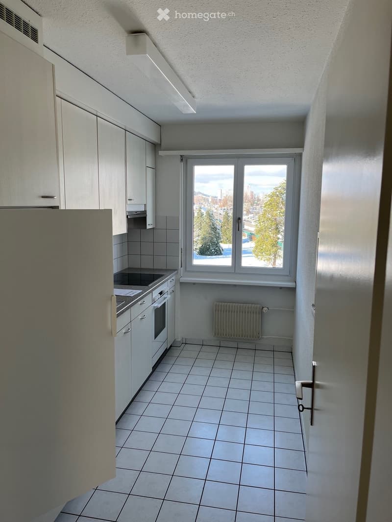 Modern kitchen with white cabinets, tiled floor, and a large window overlooking a snowy landscape.