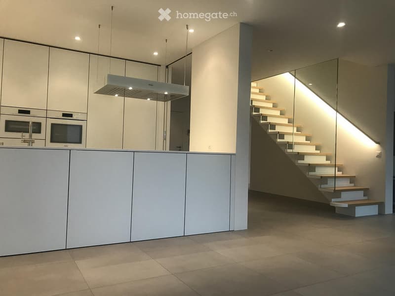 modern kitchen with white cabinets, tiled floor, glass staircase