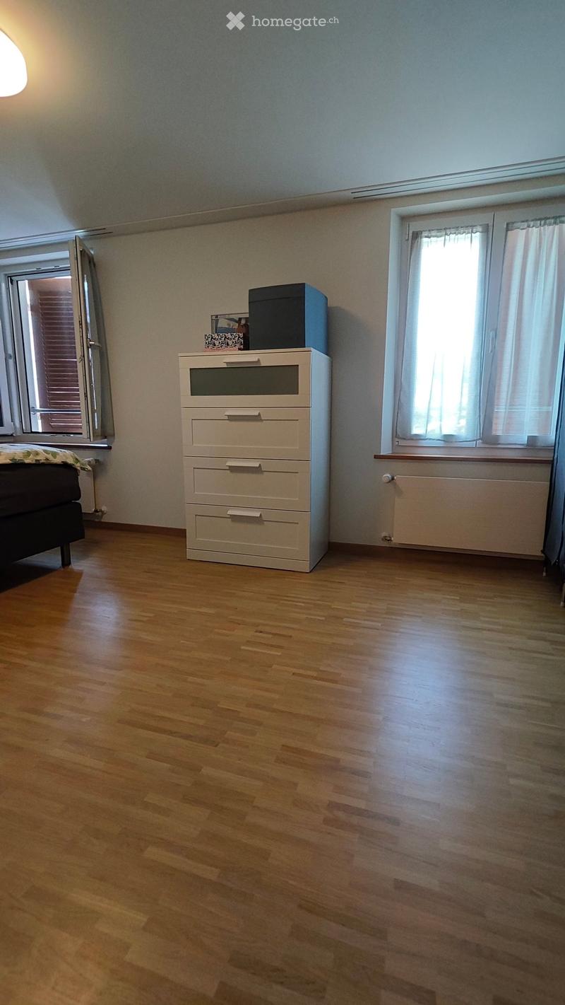 Bedroom with wooden flooring, a bed, a chest of drawers, a radiator, and a picture frame on top of the chest of drawers.