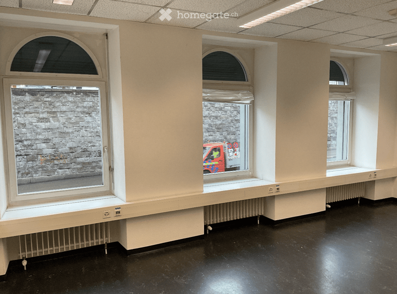 Empty room with beige walls, black floor, and multiple windows with radiators below. No furniture or equipment present.