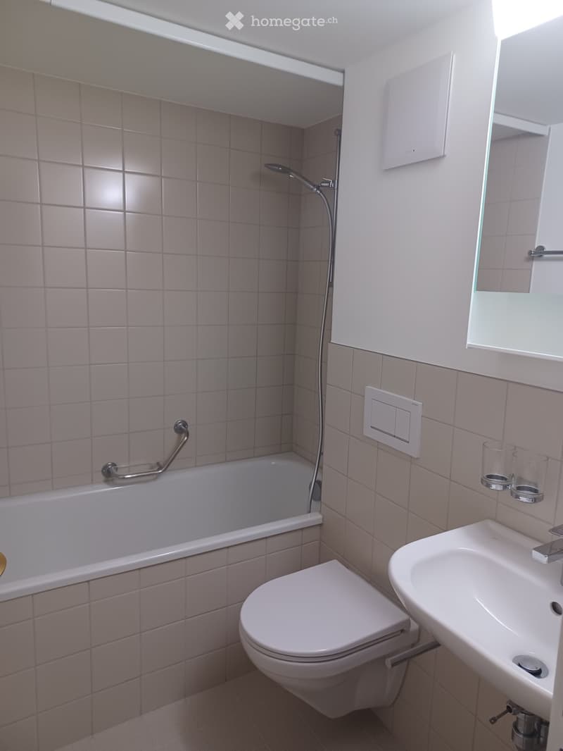 Modern bathroom with a bathtub, toilet, sink, and mirror. Light-colored tiles and a sleek design.