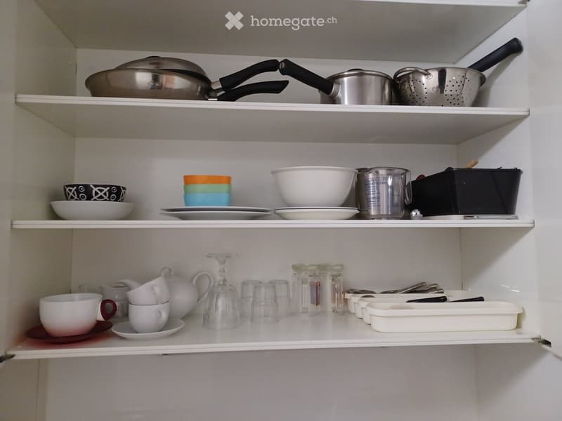 Open kitchen cabinet with neatly arranged kitchenware including pots, pans, bowls, cups, and glassware on multiple shelves.