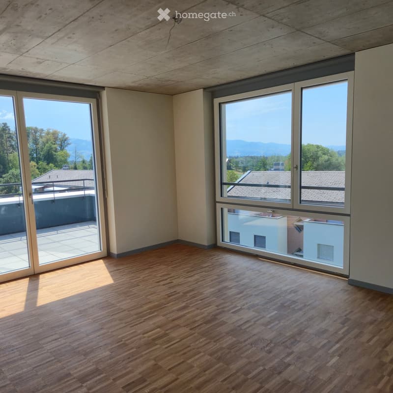 Empty room with wooden flooring, large windows, and sliding doors leading to a balcony.