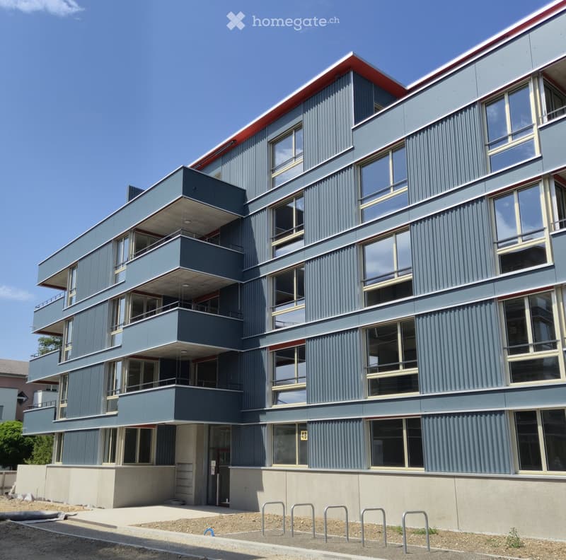 Modern multi-story building with grey and red exterior, large windows, and balconies.