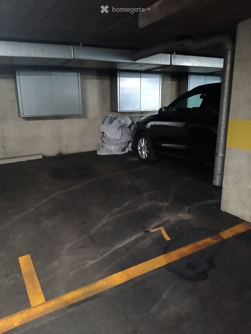Underground parking area with a parked car and some plastic bags on the floor.