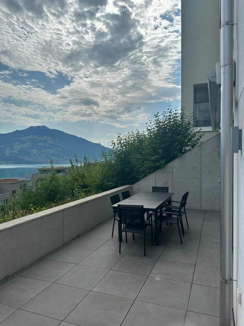 Balcony with tiled floor, table, and chairs, overlooking a scenic mountain and lake view.