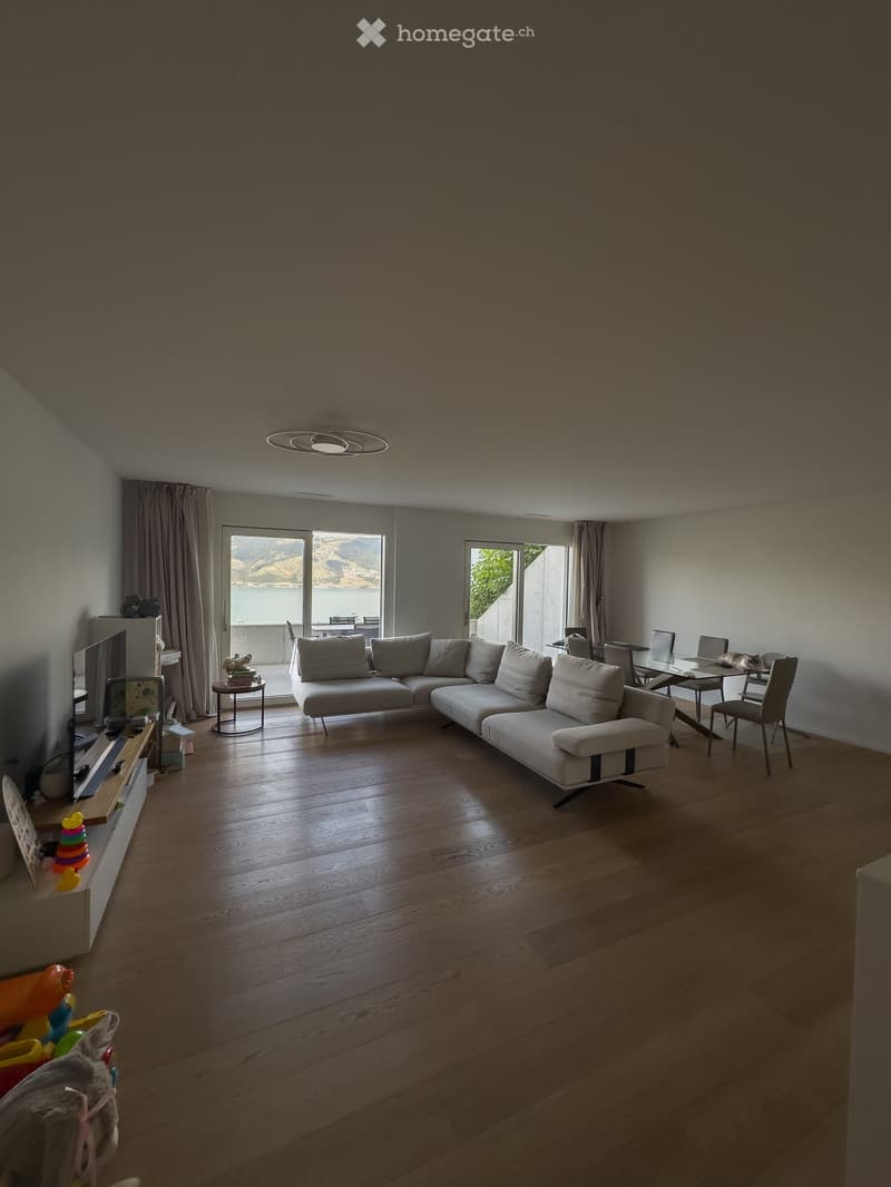 Modern living room with a large sectional sofa, coffee table, TV, and dining area with chairs and table, overlooking a scenic view.