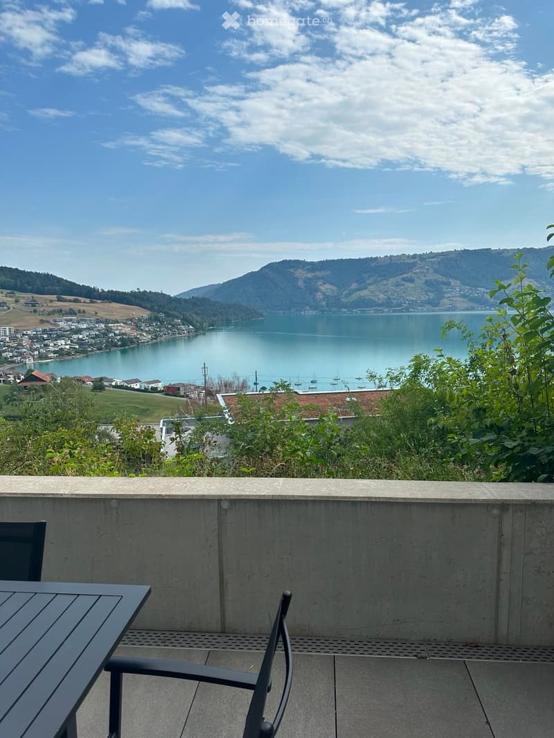 Balcony with a scenic view of a lake and surrounding hills, featuring a table and a chair.