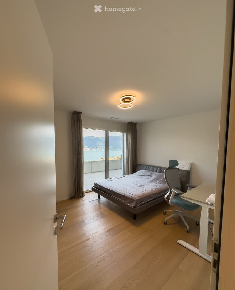 Modern bedroom with wooden flooring, large window offering a scenic view, bed, desk, and chair.