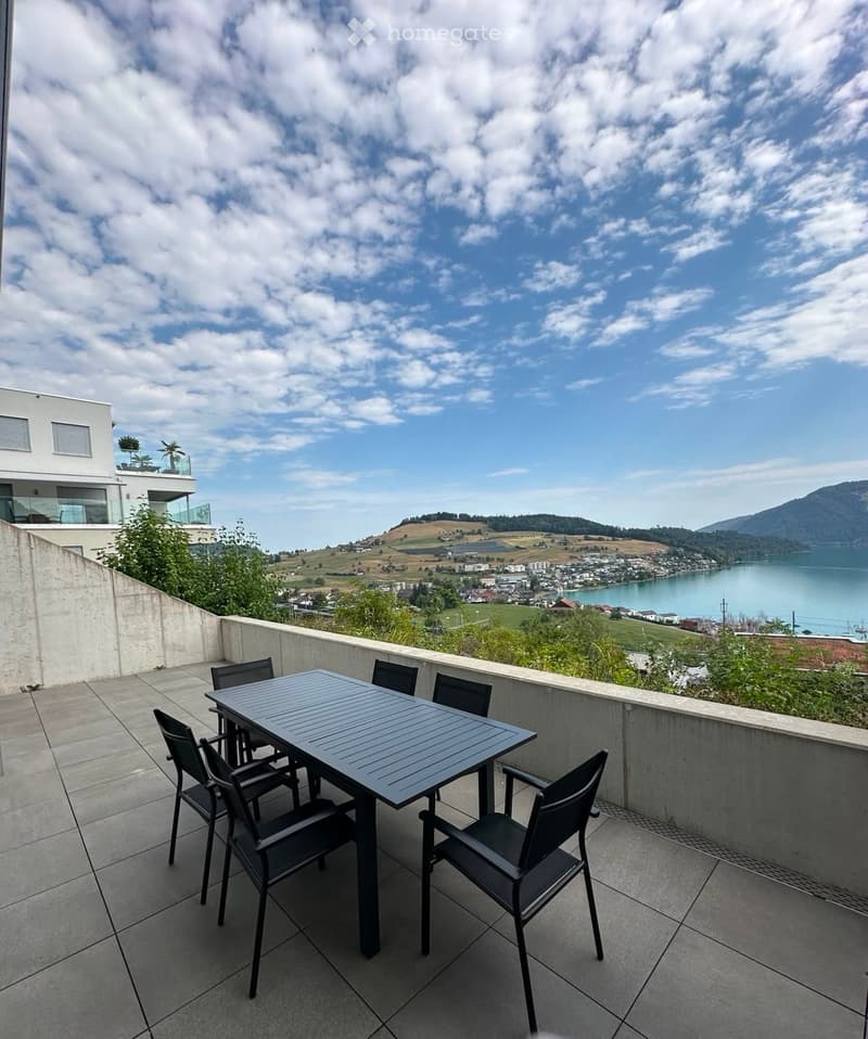 Balcony with a table and chairs, overlooking a scenic landscape with a lake and hills.