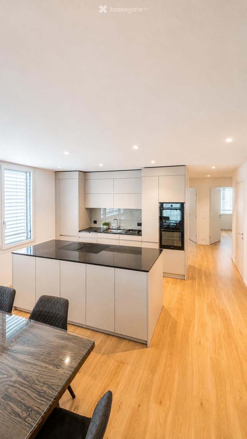Modern kitchen with white cabinets, black countertops, a central island, and a dining area with a wooden table and black chairs.