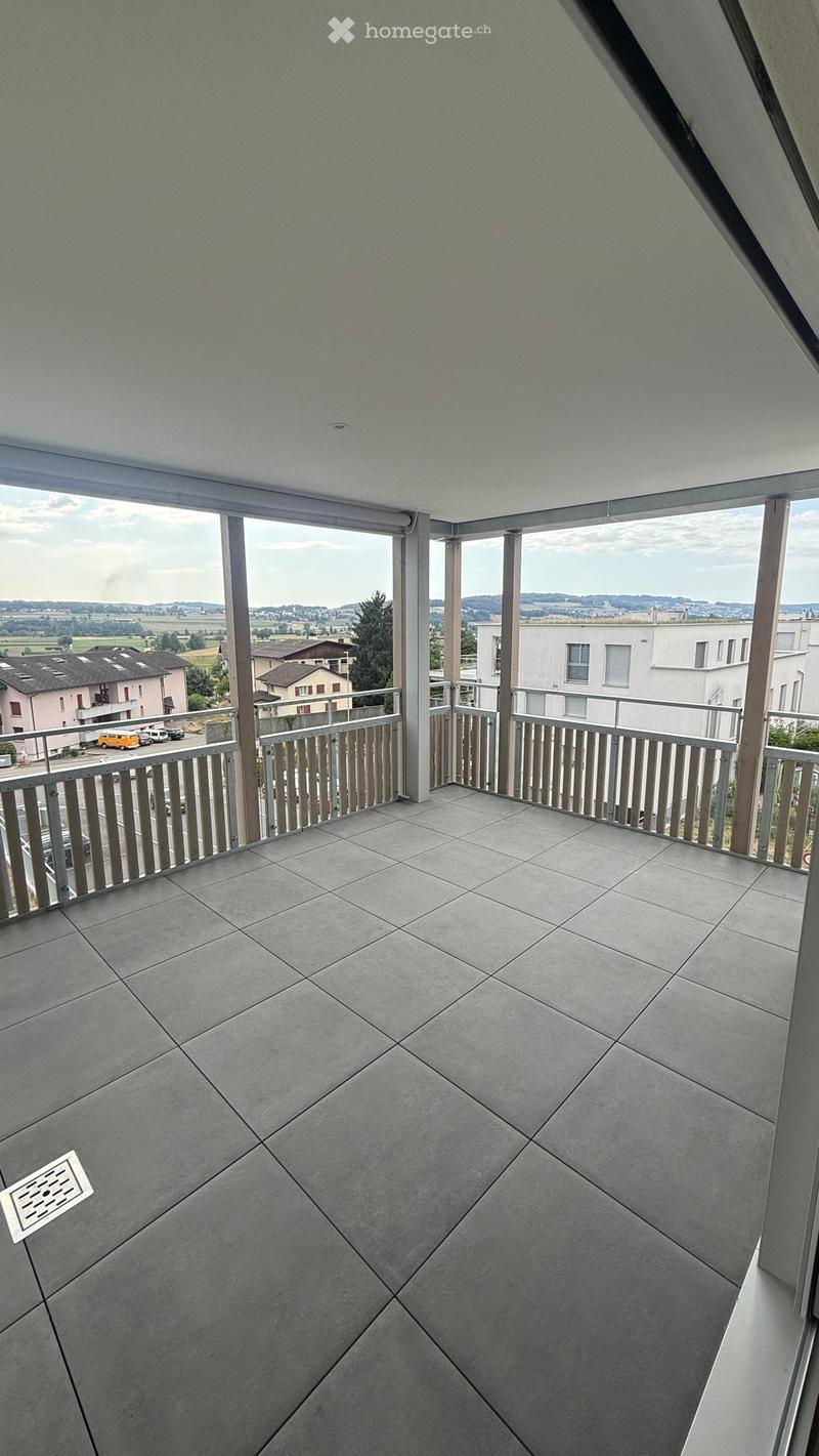 Modern balcony with grey tiled floor, metal railing, and scenic view of surrounding buildings and landscape.