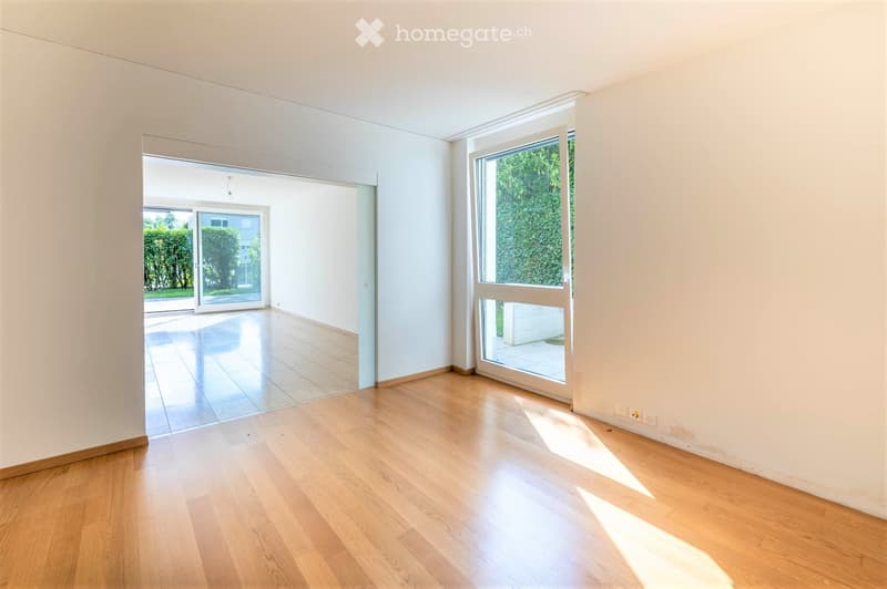 Empty room with light wooden flooring, white walls, and large sliding glass doors leading to an outdoor area.