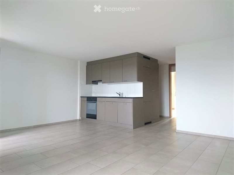 Empty kitchen with white tiled floor, grey cabinets, and white countertops. No appliances or furniture are present.