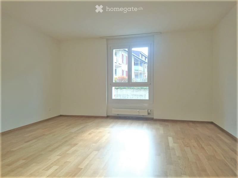 Empty room with wooden flooring, white walls, and a large window with white frame and blinds.