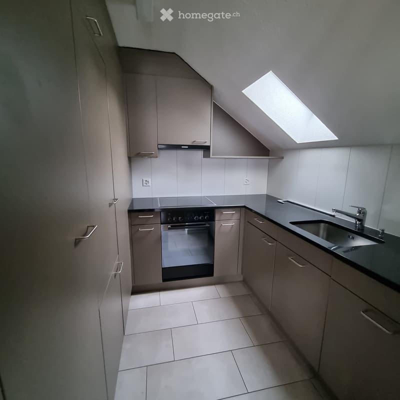Modern kitchen with grey cabinets, a stainless steel sink, and an oven. The space features a skylight and tiled flooring.