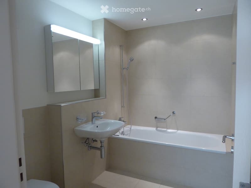 modern bathroom with white bathtub, sink with faucet, mirror, and showerhead