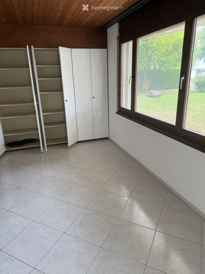 Empty room with tiled floor, white walls, large windows, and built-in white closet units.