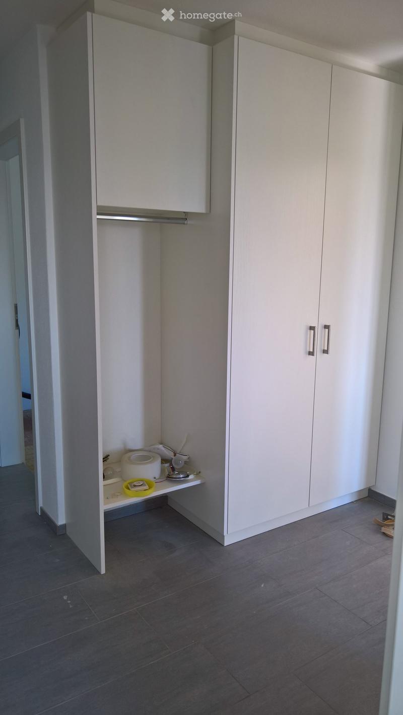 Empty hallway with white built-in cabinets, a small shelf with a few items, and a dark tiled floor.