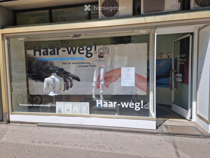 Storefront with large glass windows displaying advertisements for permanent hair removal, including mannequins and illustrations.