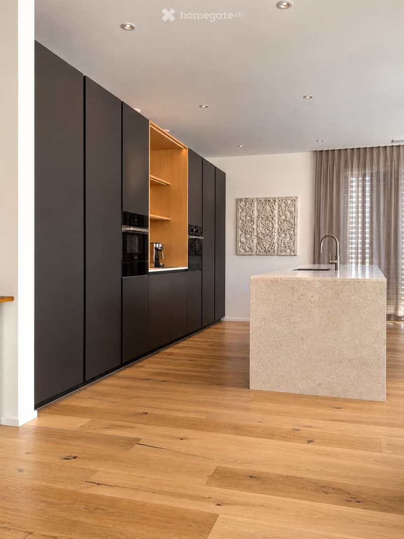 Modern kitchen with dark cabinets, light wooden floor, central island with marble countertop, sink, faucet, coffee maker, and built-in oven.
