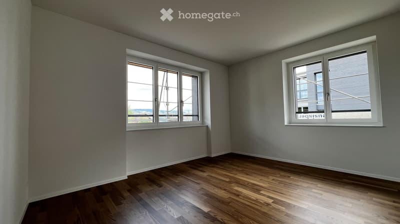 Empty room with wooden flooring and large windows, no furniture or equipment.