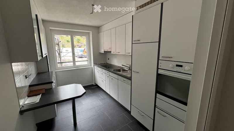 Modern kitchen with white cabinets, black countertops, a sink, and an oven. A small round table is placed near the window.