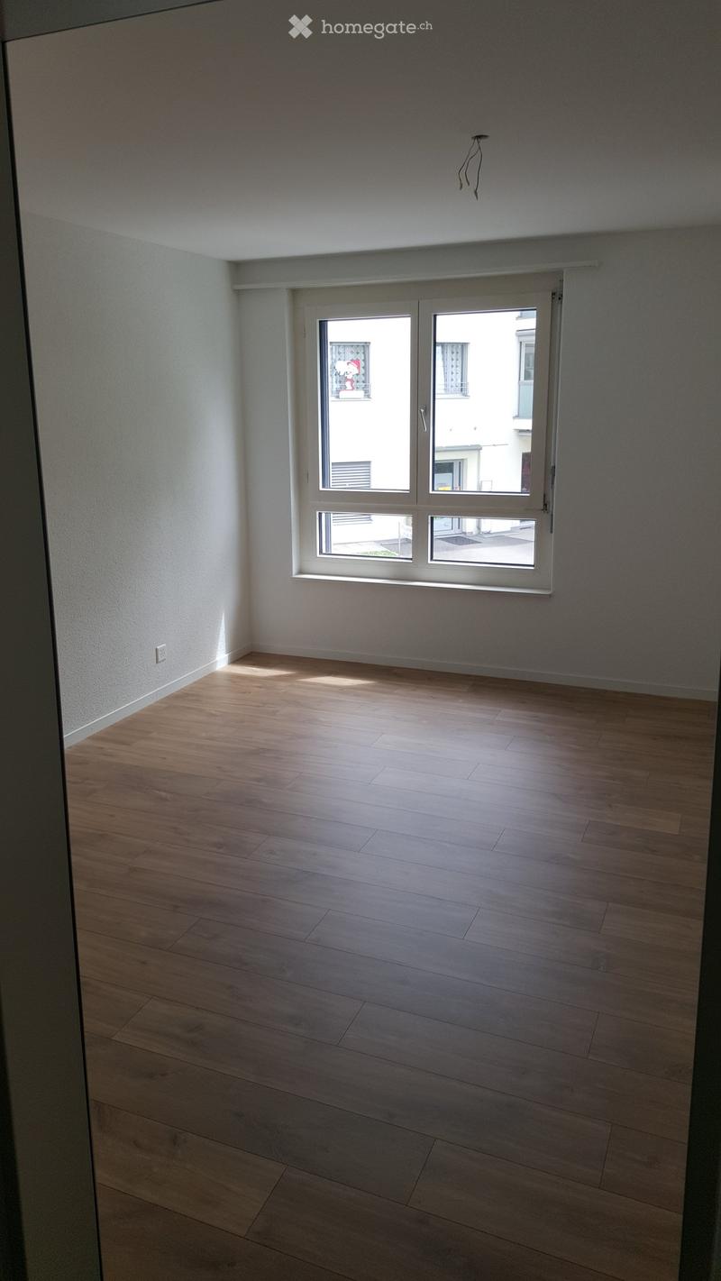 Empty room with wooden flooring and large windows letting in natural light. The walls are painted white, and the space is completely unfurnished.