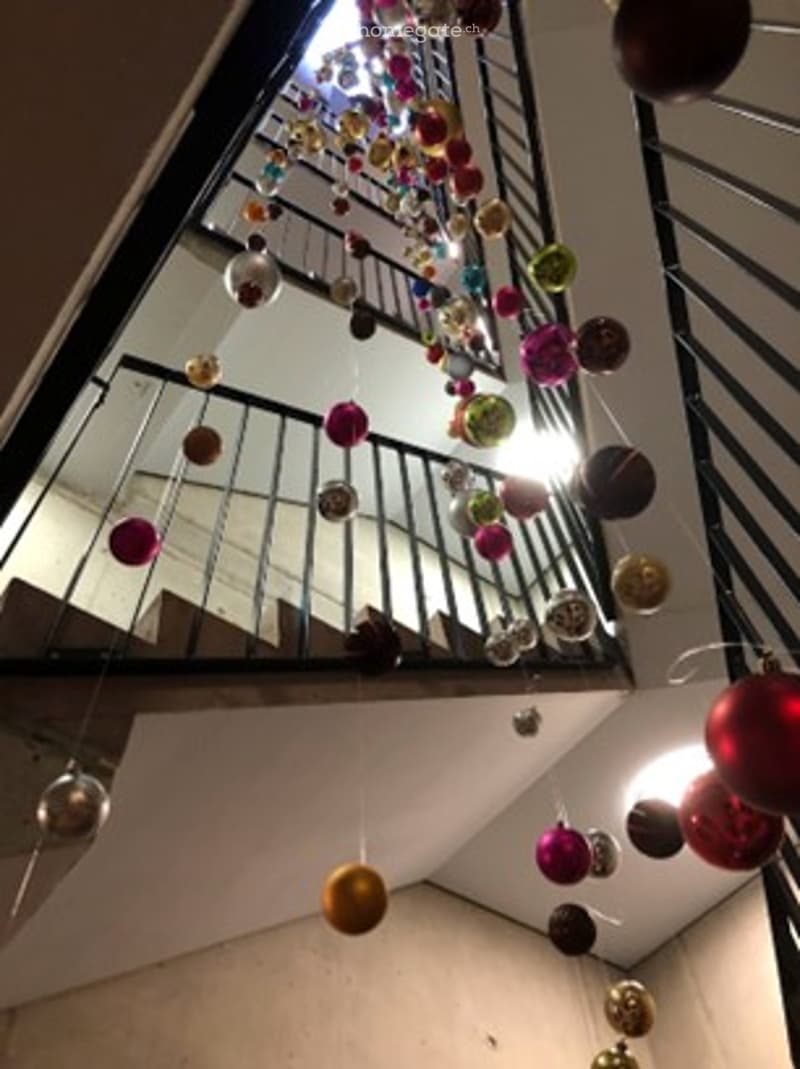 A modern hallway with a staircase, decorated with colorful hanging ornaments and lights.
