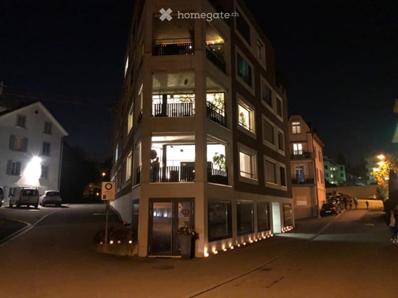 Multi-story residential building at night with illuminated windows and balconies, surrounded by parked cars and streetlights.