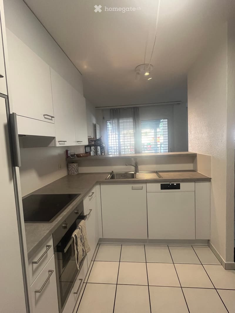 Modern kitchen with white cabinets, stainless steel appliances, tiled floor, and a window with blinds.