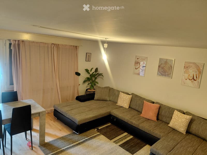 Living room with a grey sectional sofa, wooden dining table, chairs, a small plant, and wall art.