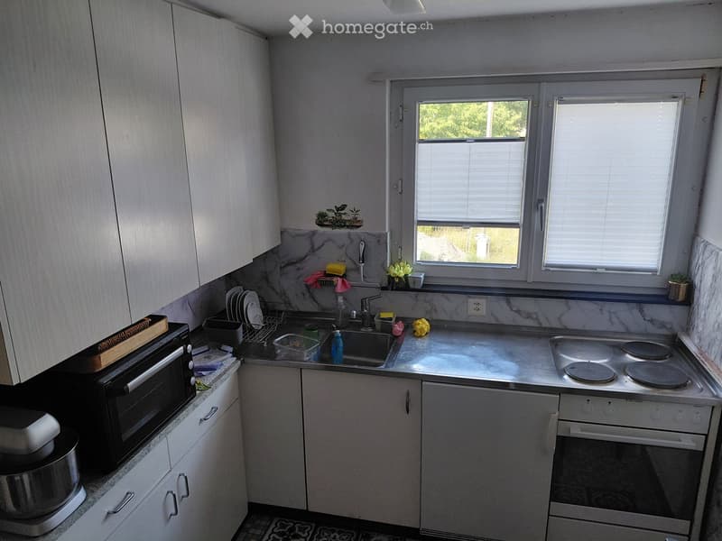 Modern kitchen with white cabinets, marble countertops, and stainless steel appliances including a microwave, oven, and sink.