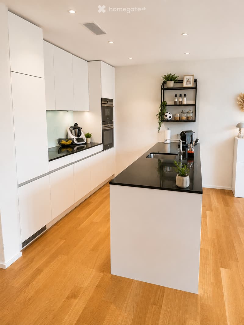 Modern kitchen with white cabinets, black countertops, wooden flooring, and various appliances including a blender, oven, and sink.