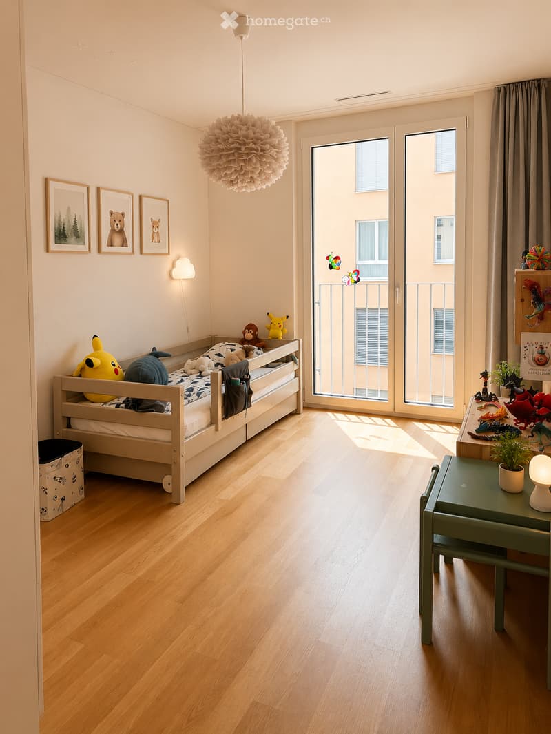 Bright, modern bedroom with wooden flooring, a single bed with colorful bedding, a small green table with a lamp, and various toys and decorations.