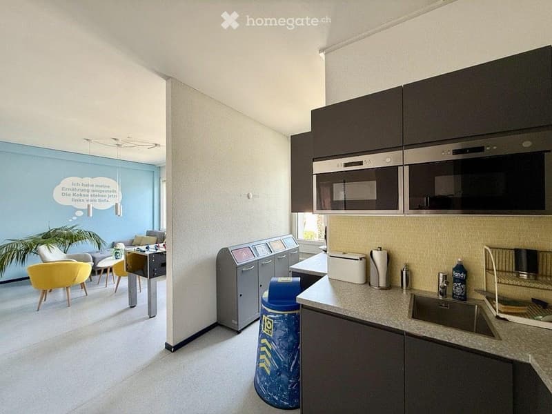Modern kitchen and living area with grey cabinets, stainless steel appliances, a microwave, oven, sink, and a living space with a sofa, chairs, and a table.