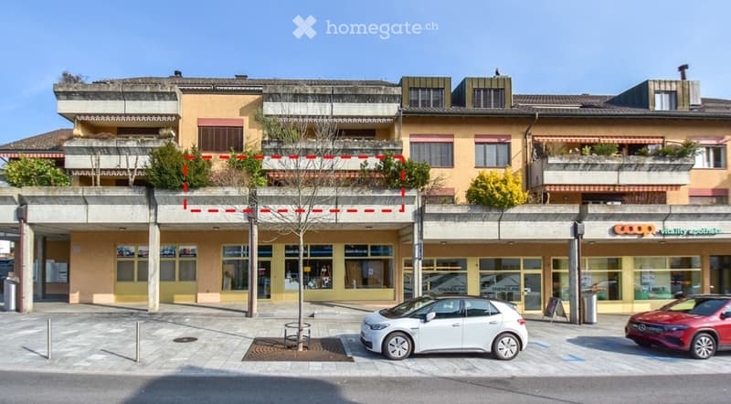 Terraced building with 2nd floor outlined. The ground floor has commercial space. There is a balcony on the second floor, indicated by red lines. Below are two cars parked in front.