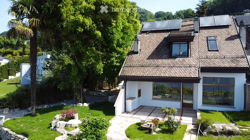 Modern two-story house with solar panels on the roof, large windows, and a well-maintained garden with a stone pathway and various plants.