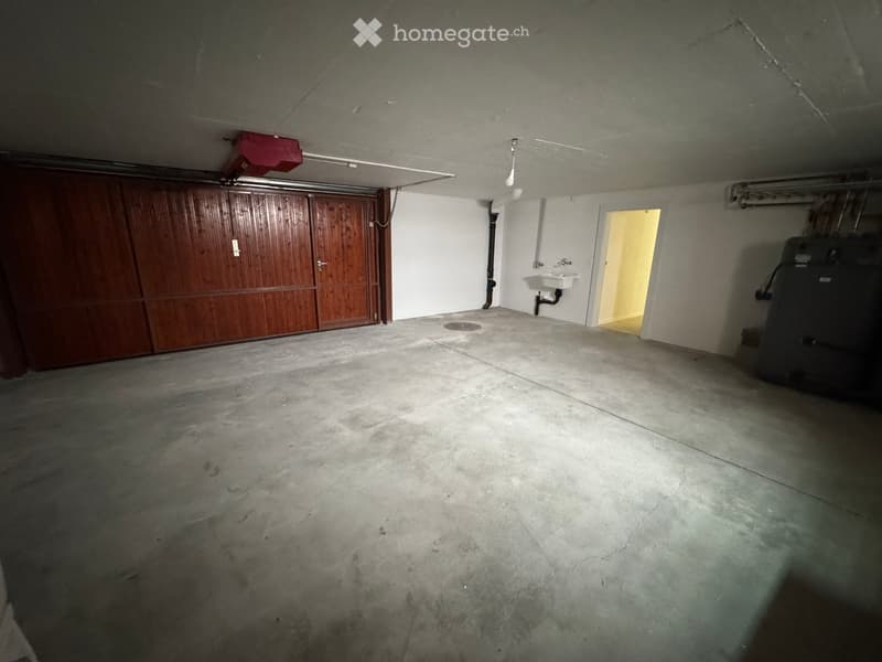 Empty garage with concrete floor, wooden garage door, small sink, and a doorway leading to another room.