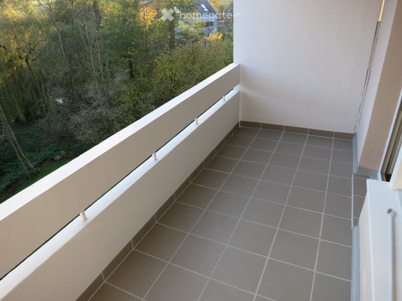 Balcony with tiled floor, white railing, and view of greenery and trees.